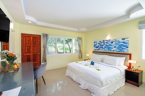 A hotel room with a bed, a desk, a chair, a window with curtains, and a painting on the wall. - Oceanview Bungalows by EAT, Karon Beach (Karon)