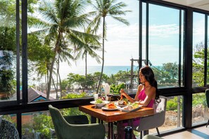A dining area with a view of the sea and palm trees, featuring a table with plates of food and a person dining. - Oceanview Bungalows by EAT, Karon Beach (Karon)
