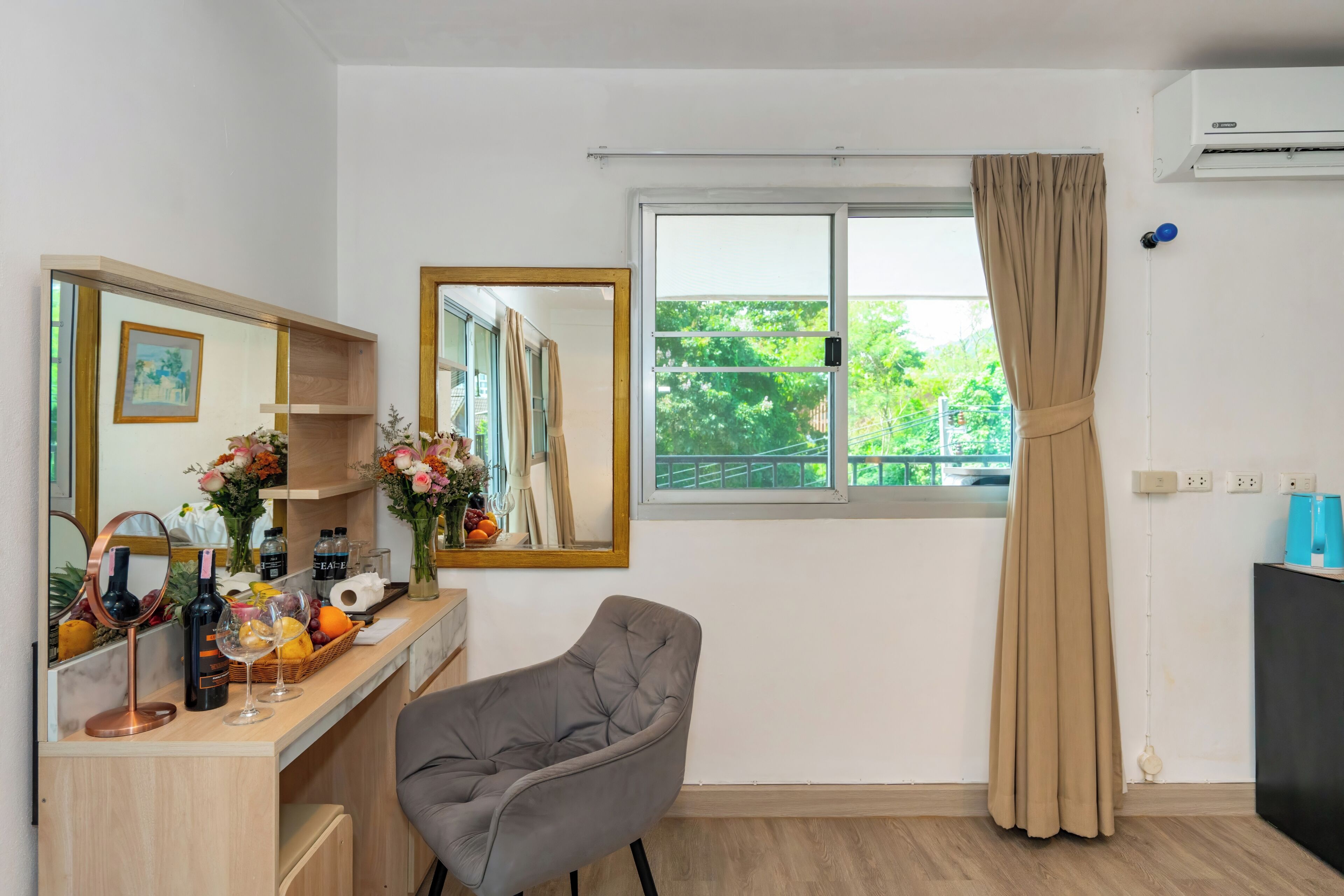 A room with a wooden desk, a chair, a large mirror, a window with curtains, and an air conditioning unit.