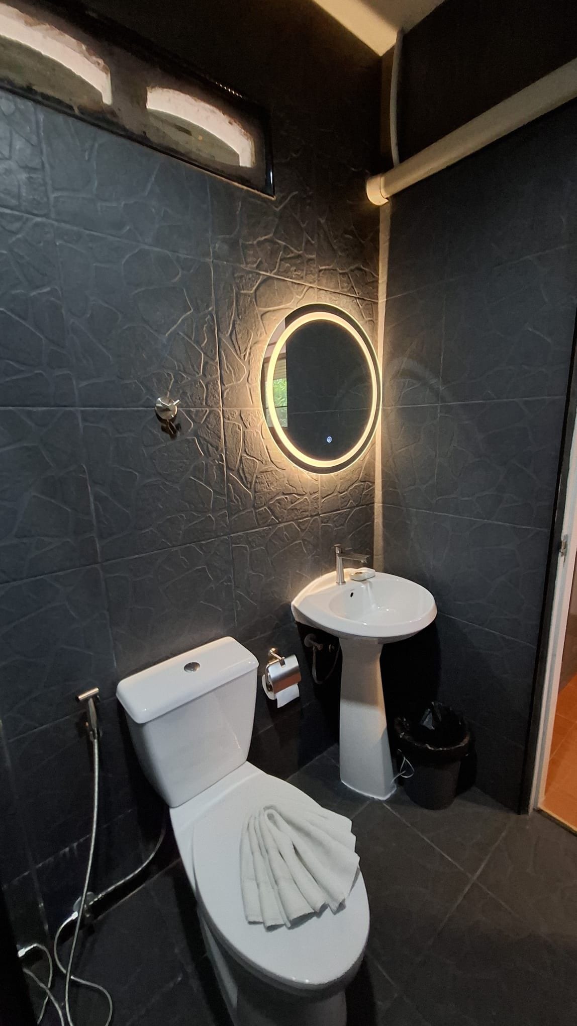 A modern bathroom with a toilet, sink, and a wall-mounted mirror with a circular light.