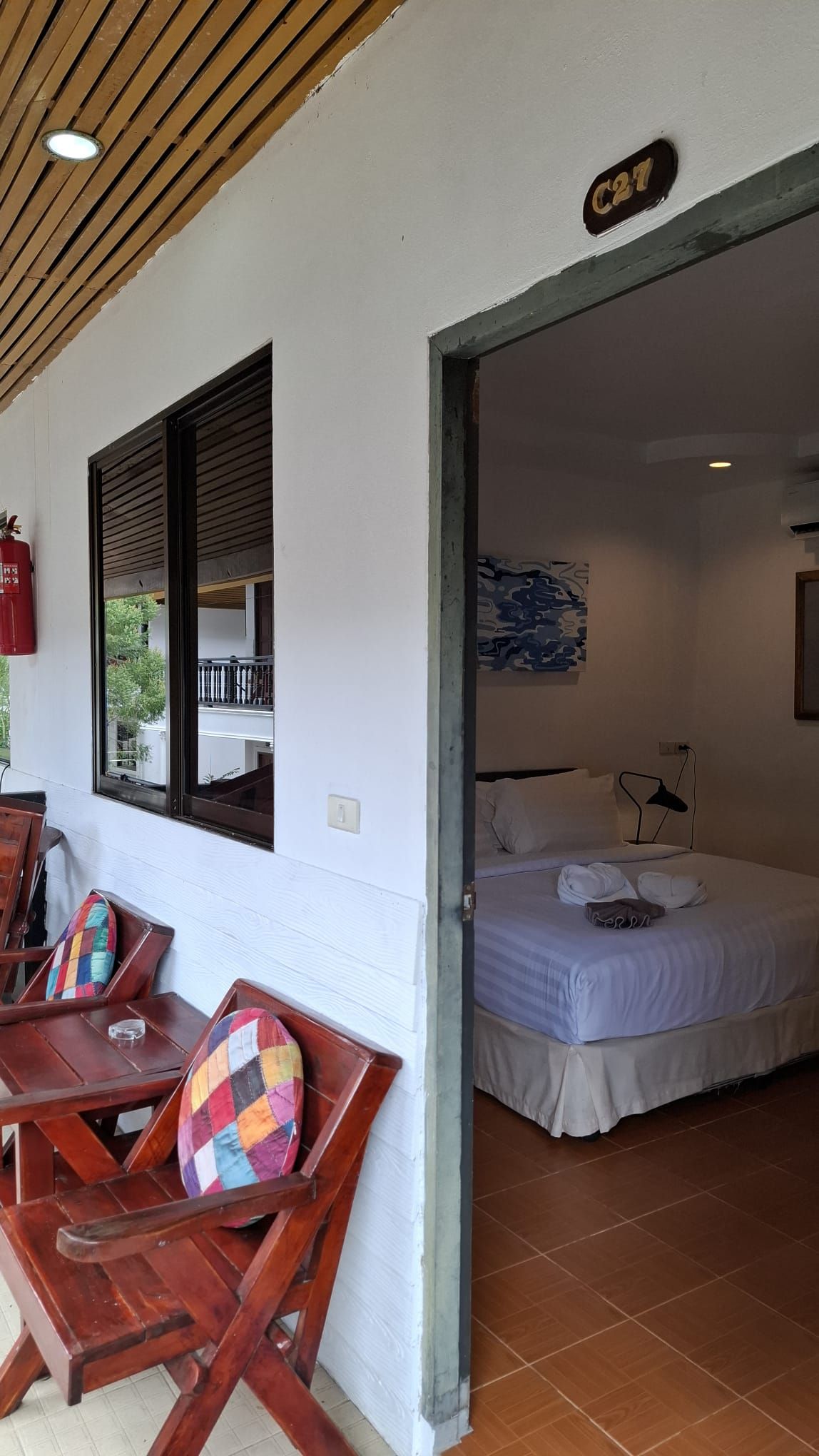 A room with a bed, a window with blinds, a wooden ceiling, and a sign above the door.
