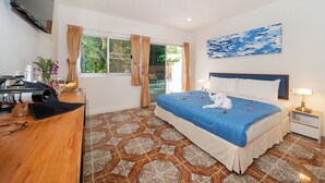 Una habitación de hotel con cama, escritorio, televisor y ventana con cortinas.
