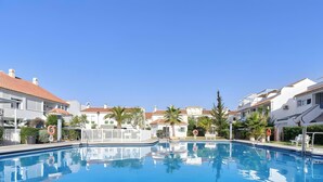 Una piscina circondata da edifici con tetti in tegole rosse e pareti bianche, palme e cielo azzurro terso.