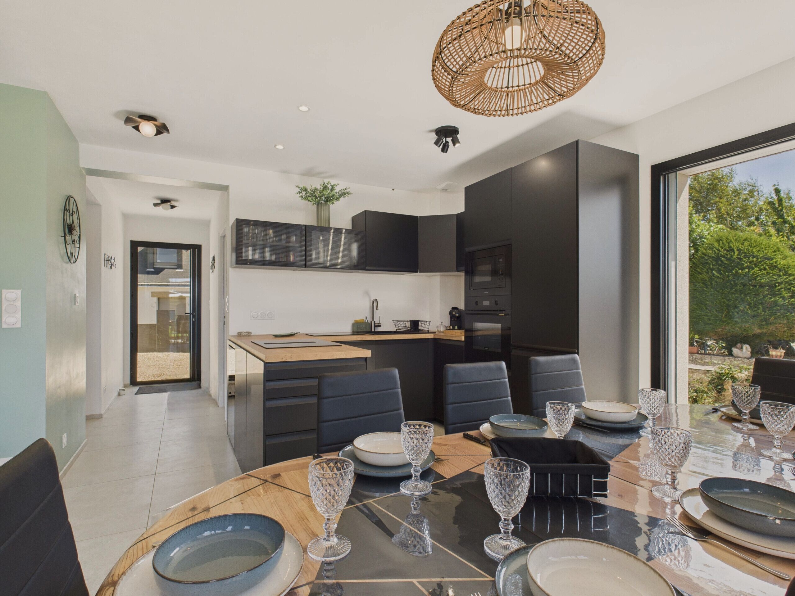 A modern kitchen with dark cabinetry, a wooden island, and a dining area with a round table set for six.