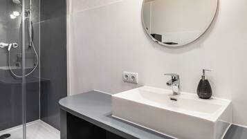A modern bathroom with a glass-enclosed shower, a white sink with a mirror above, and a black soap dispenser.