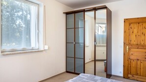 Um quarto com cama, roupeiro com porta de correr, guarda-roupa de madeira e janela.