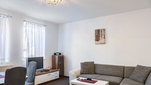 Uma sala de estar com sofá, televisão, escrivaninha e uma cadeira.