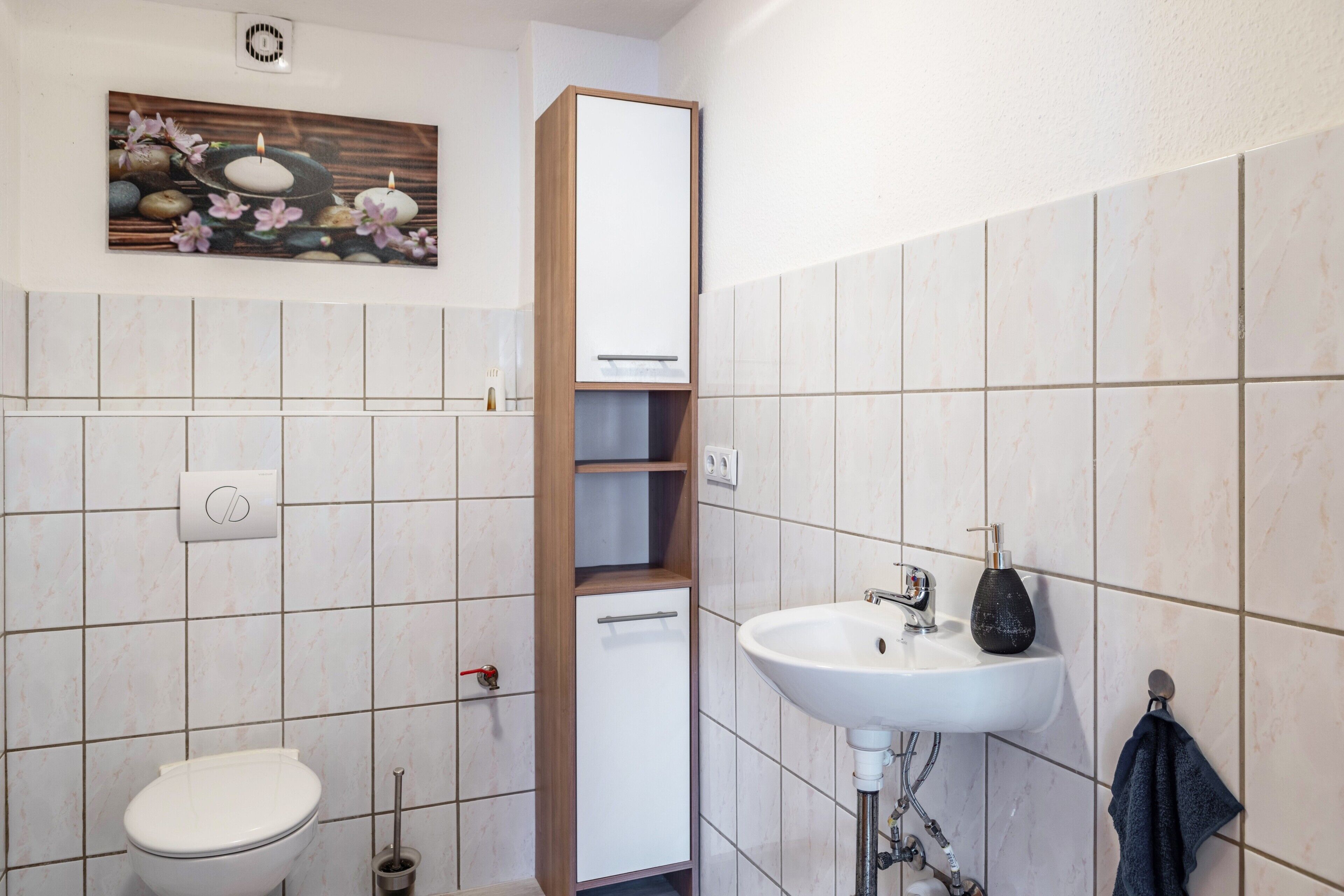 Et badeværelse med toilet, vask, skab og en dekorativ vægdekoration.