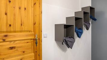 A wooden door with a brass handle, a white wall with a light switch, and three grey storage units with folded towels.
