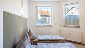 A bedroom with two beds, a window with a view, and a radiator.