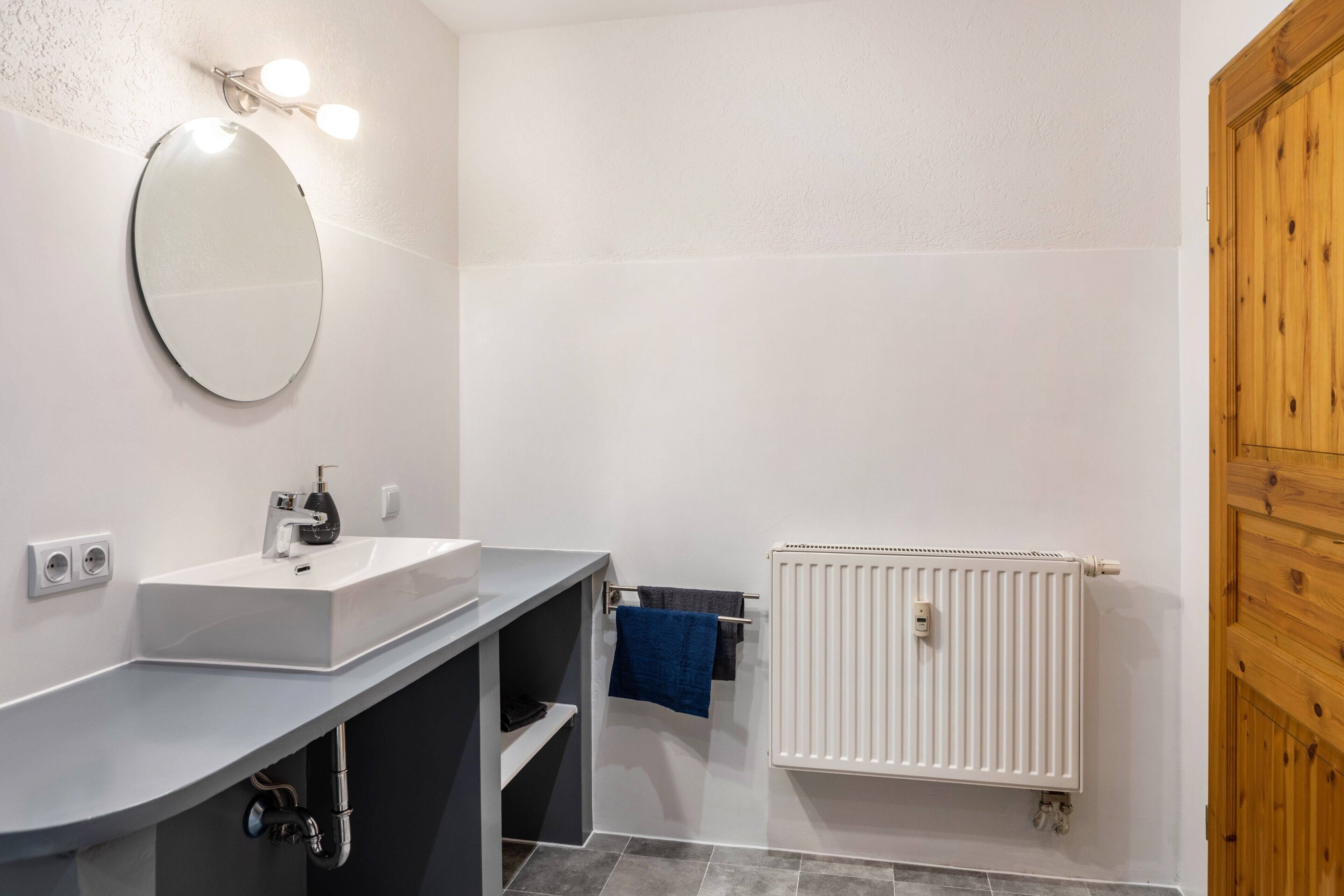 A bathroom with a white sink, mirror, and radiator.