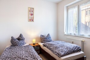 Ein Schlafzimmer mit zwei Betten, einem Nachttisch, einer Lampe, einem Fenster mit Vorhängen und einer Wanddekoration mit Herzmuster.