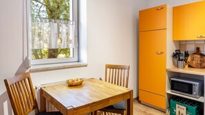 Uma cozinha com mesa de madeira, cadeiras, janela com cortinas e uma geladeira laranja vibrante.