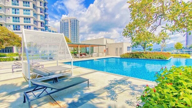 A rooftop pool area with lounge chairs and a covered seating area, surrounded by greenery and modern buildings in the background. - Teega Residence (Iskandar Puteri)