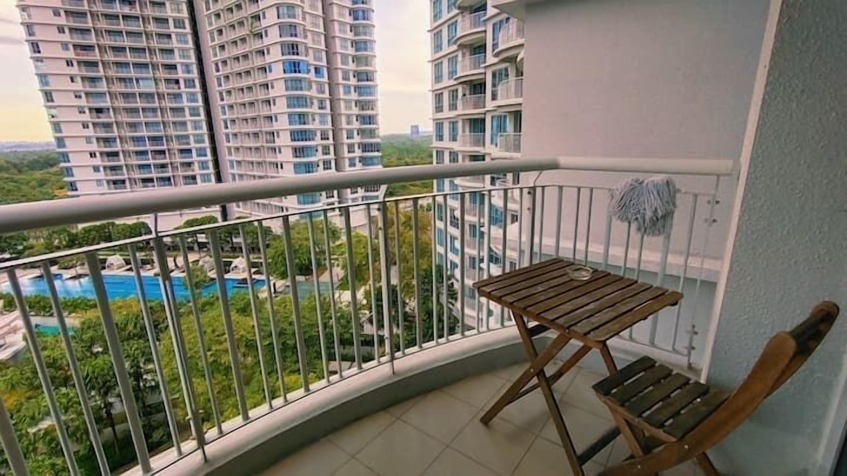 Un balcone con tavolo e sedia in legno, affacciato su una piscina e grattacieli.