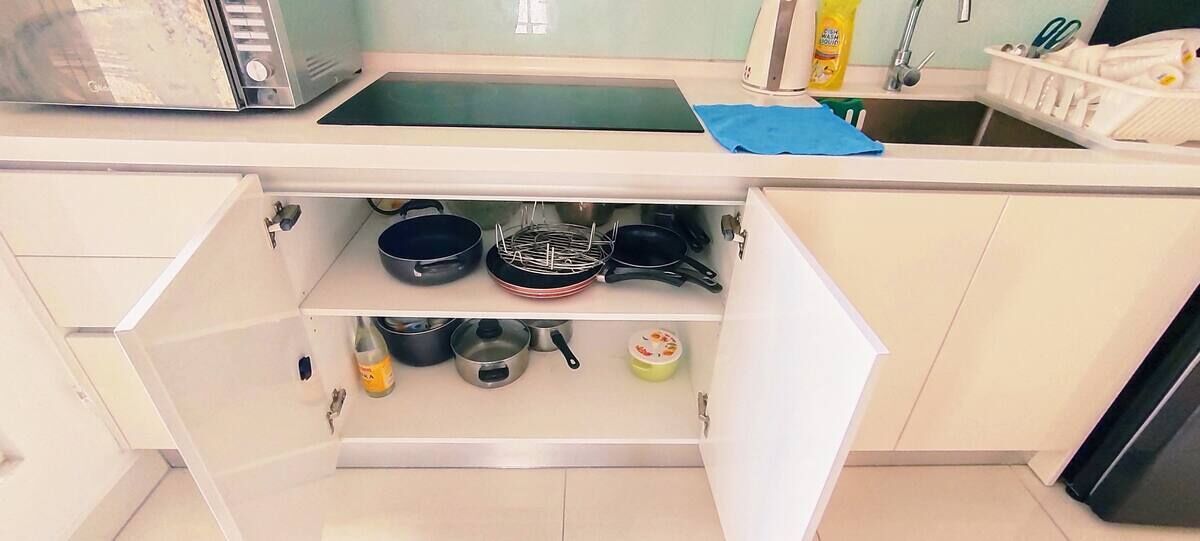A kitchen with a microwave, sink, and various pots and pans stored in a cabinet.