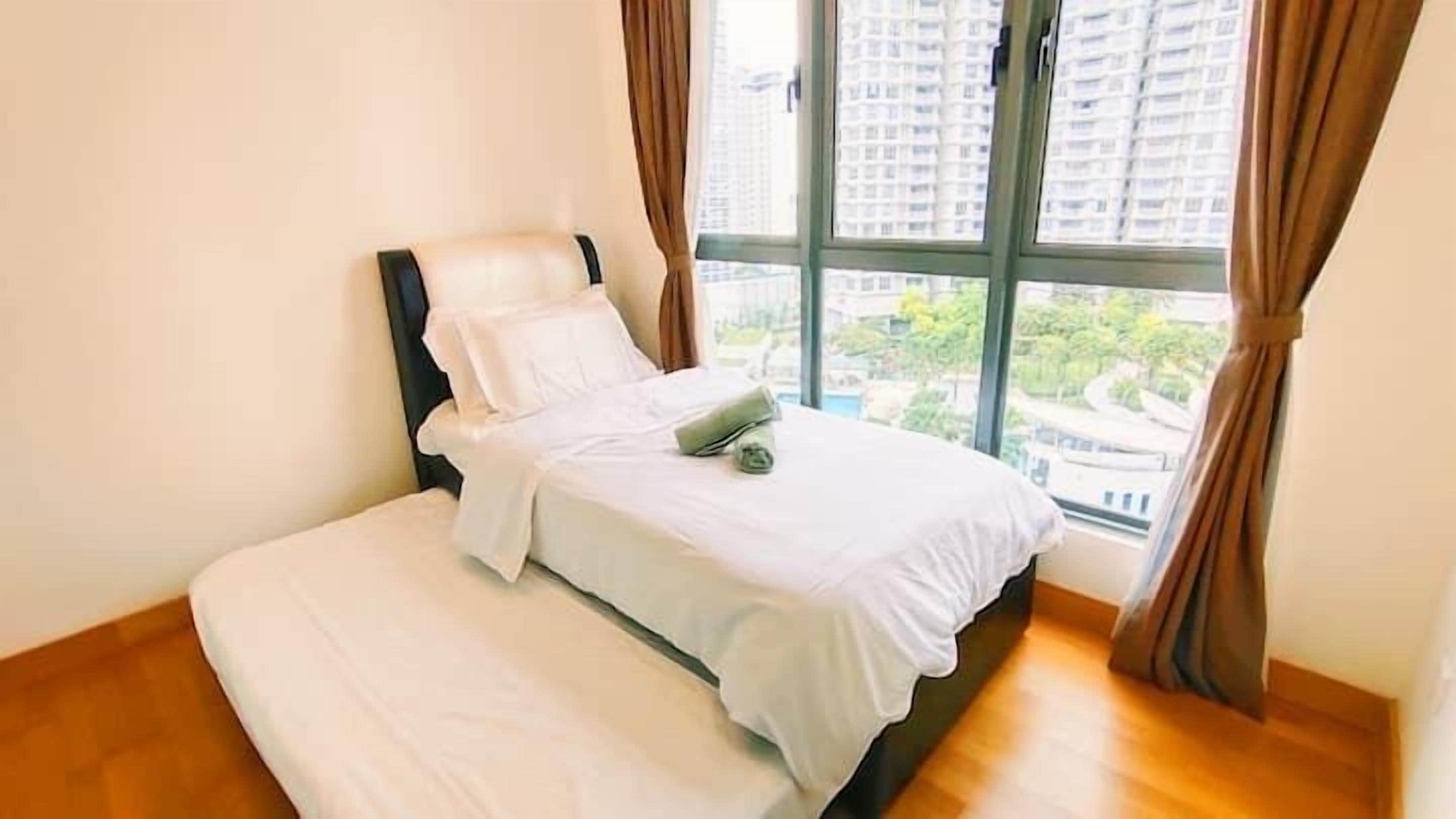 A neatly made bed with white linens and a rolled towel, a window with curtains, and a view of a cityscape.