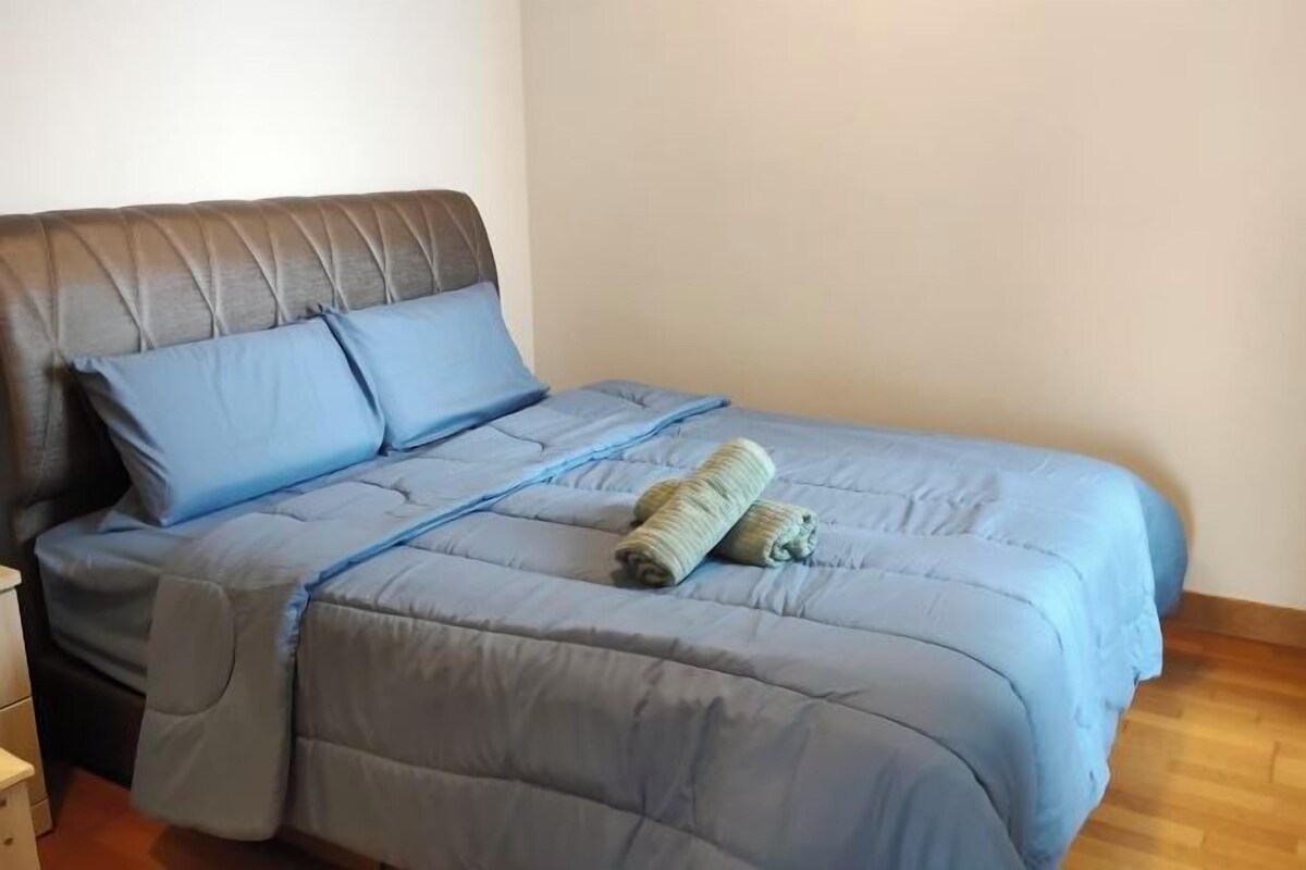 A bed with a grey headboard and blue bedding, including a blue pillow and two rolled towels.