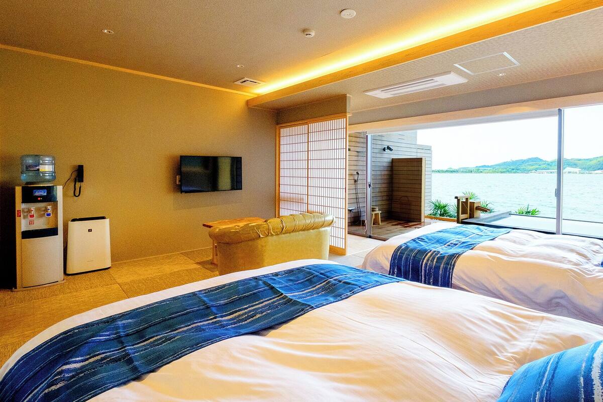 A hotel room with two beds, a water dispenser, a TV, and a large window with a view of a lake.