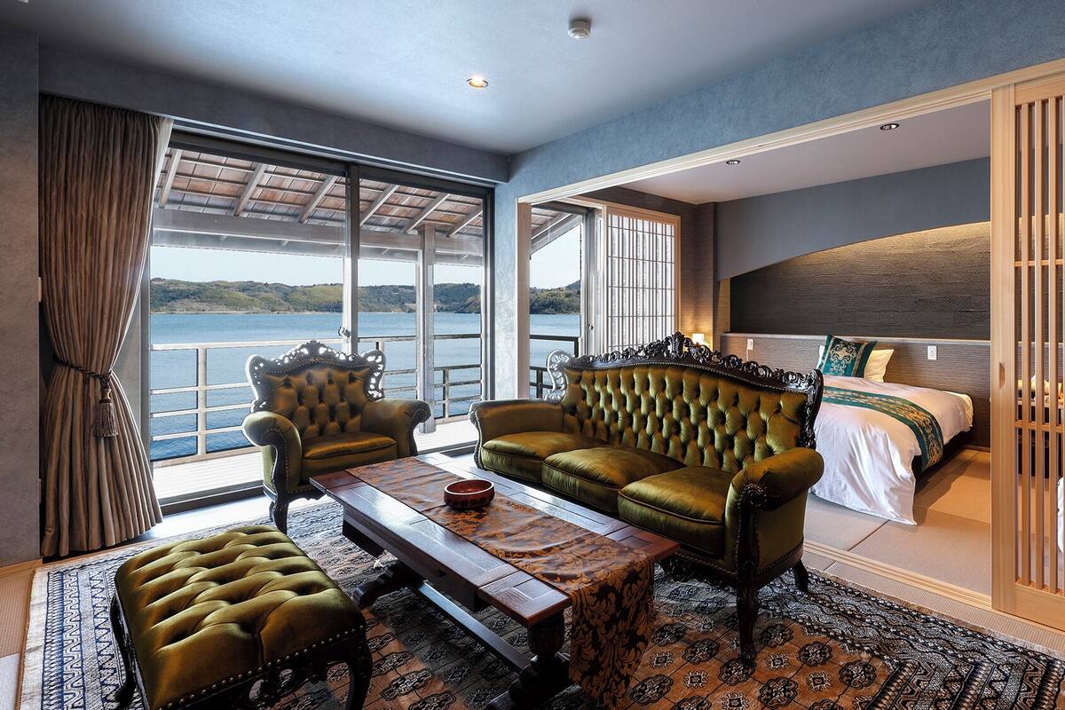 A room with a large window, a sofa, a bed, and a table.