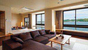 A modern hotel room with a large sofa, a dining area, and a view of a lake. - Sennentei (Yurihama)