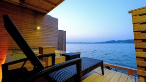 A wooden deck with wicker furniture overlooking a body of water. - Sennentei (Yurihama)