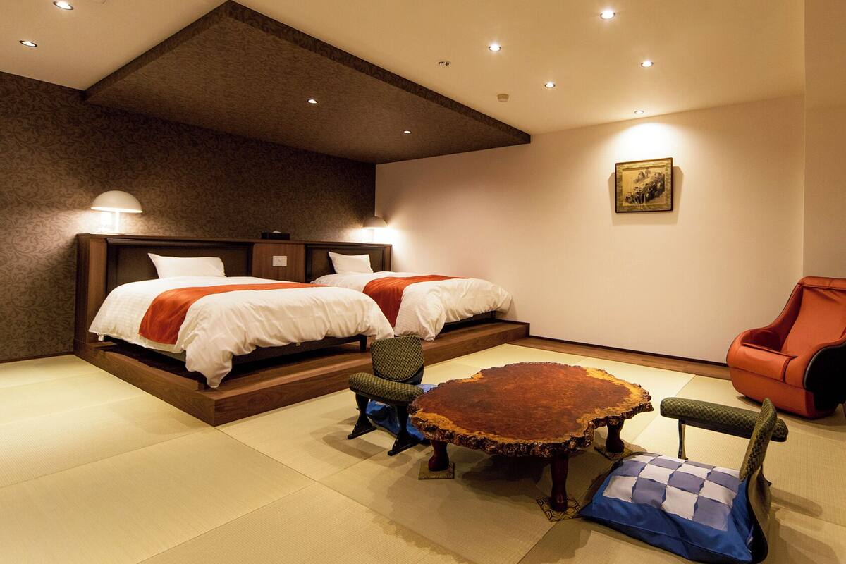 A hotel room with two beds, a dining table, and a chair.