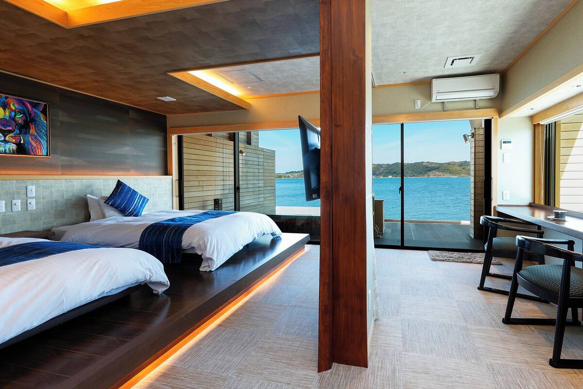 A modern room with two beds, a desk, and a large window overlooking a body of water.