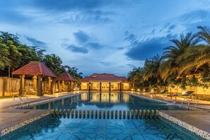 A swimming pool with a tiled pattern, surrounded by lounge chairs and palm trees, with a building in the background. - Sterling Hibis Vellore (Vellore)