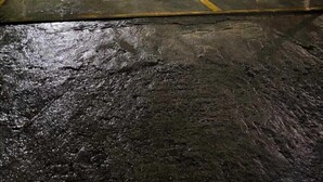 A nighttime view of a gated parking area with a wet surface, possibly after rain.
