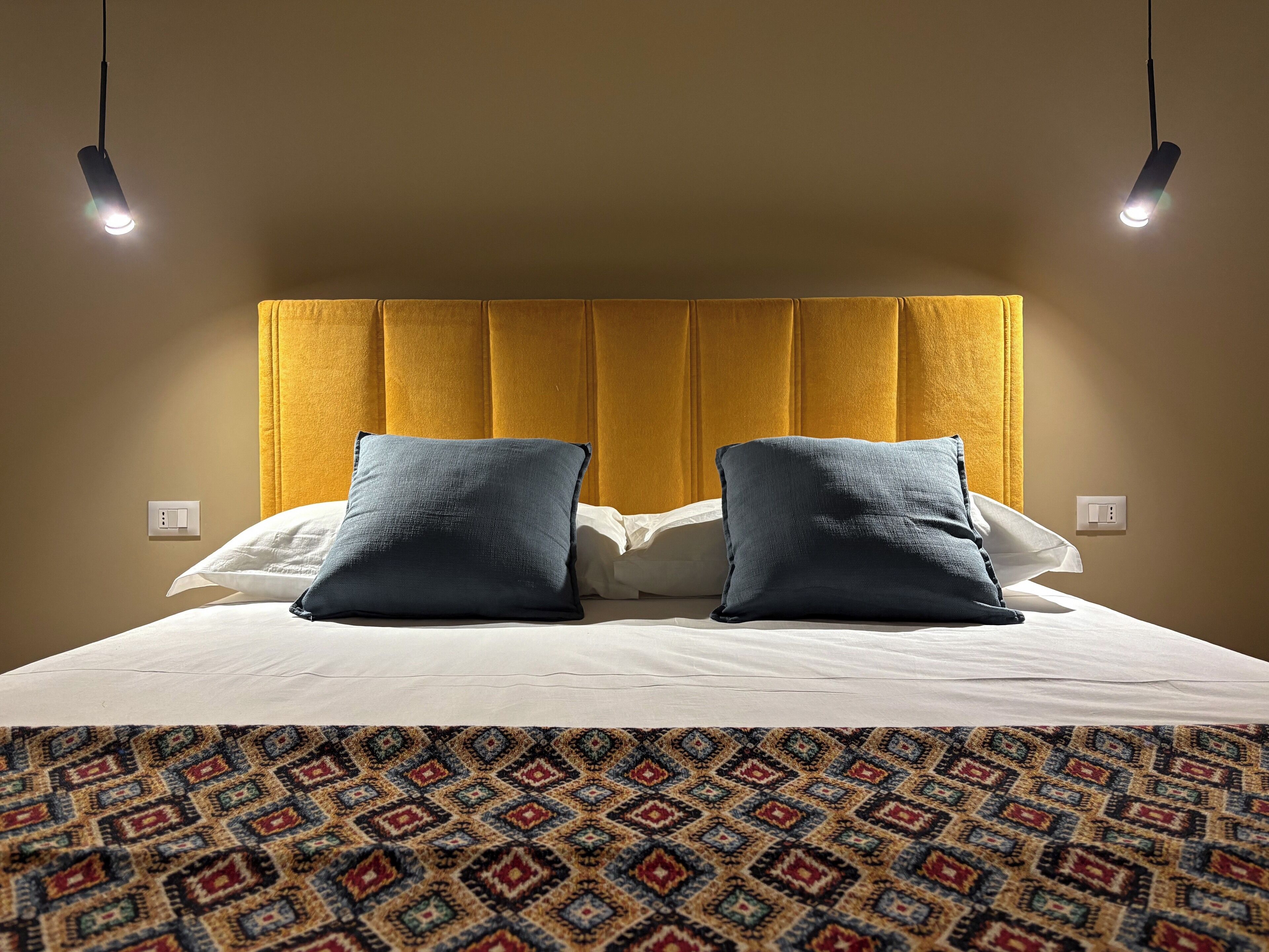 Ein Hotelzimmer mit einem großen Bett, zwei Kissen, einem gemusterten Teppich und einem gelben Kopfteil.