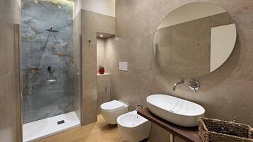 Un baño moderno con ducha envuelta en vidrio, espejo redondo, lavamanos y un bidé.