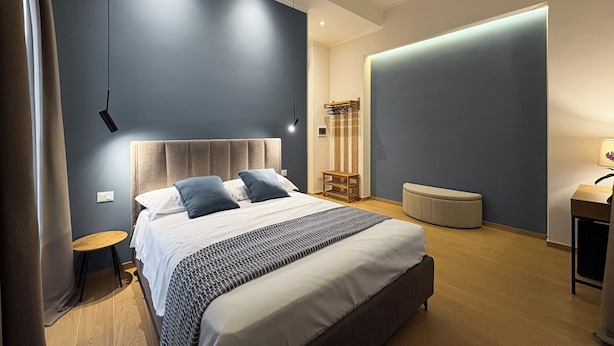 Une chambre à coucher moderne avec un grand lit, des tables de chevet, une petite table ronde et un luminaire fixé au mur.