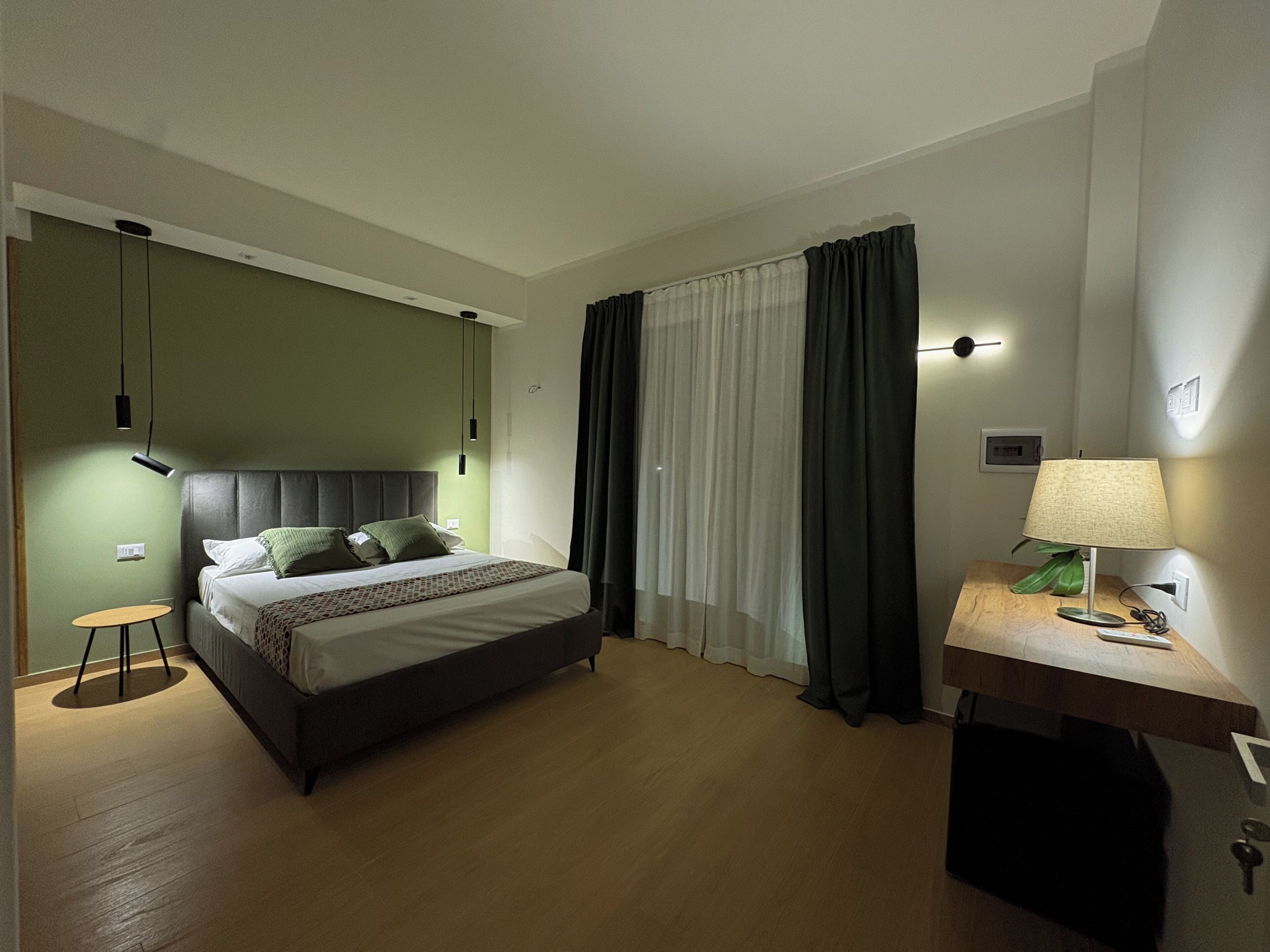 A hotel room with a bed, a desk, a lamp, and a window with curtains.