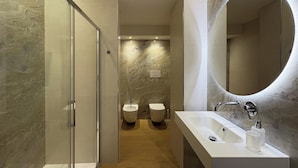 Une salle de bain moderne avec une douche à parois de verre, un grand miroir et deux toilettes.