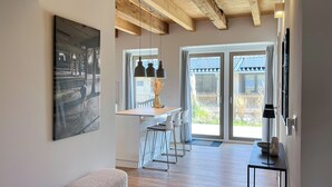 A modern kitchen with a wooden ceiling, a dining area with bar stools, and a large window with a view of a fence.
