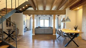 A spacious living area with a wooden staircase, a dining table with chairs, and a large window providing natural light.