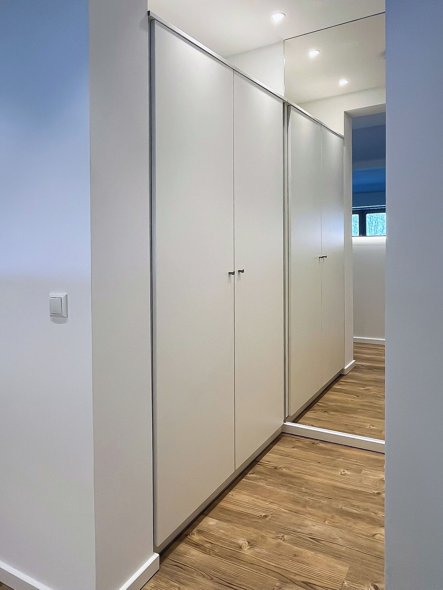 Un couloir avec un placard aux portes miroir et un plancher en bois.