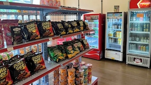 A snack display with various packaged snacks, a Coca-Cola refrigerator, and a Prost refrigerator in a store. - Anders Permata Millenium (Curug)