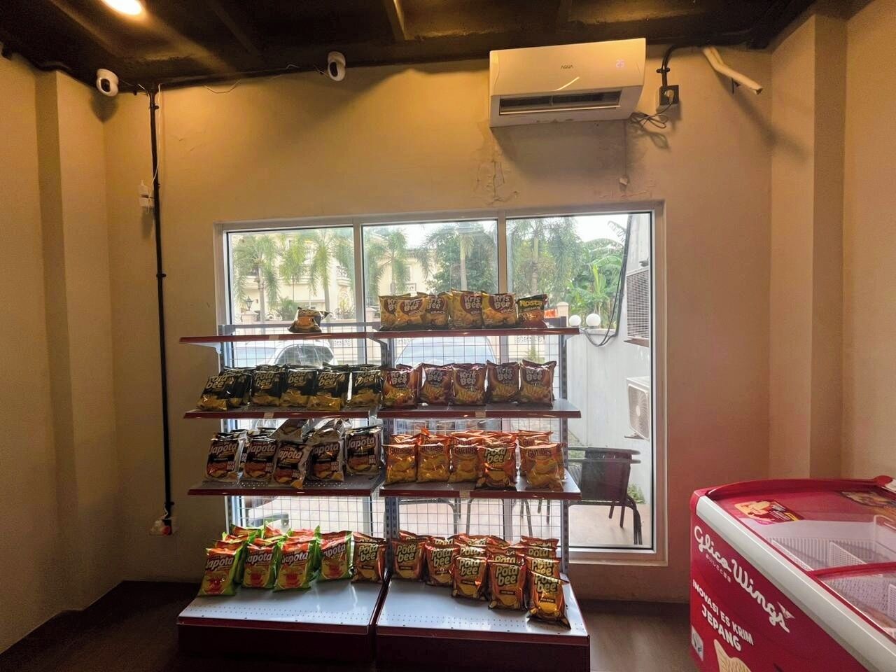 A snack display with various packaged foods, a window with a view of palm trees, and an air conditioning unit on the wall.