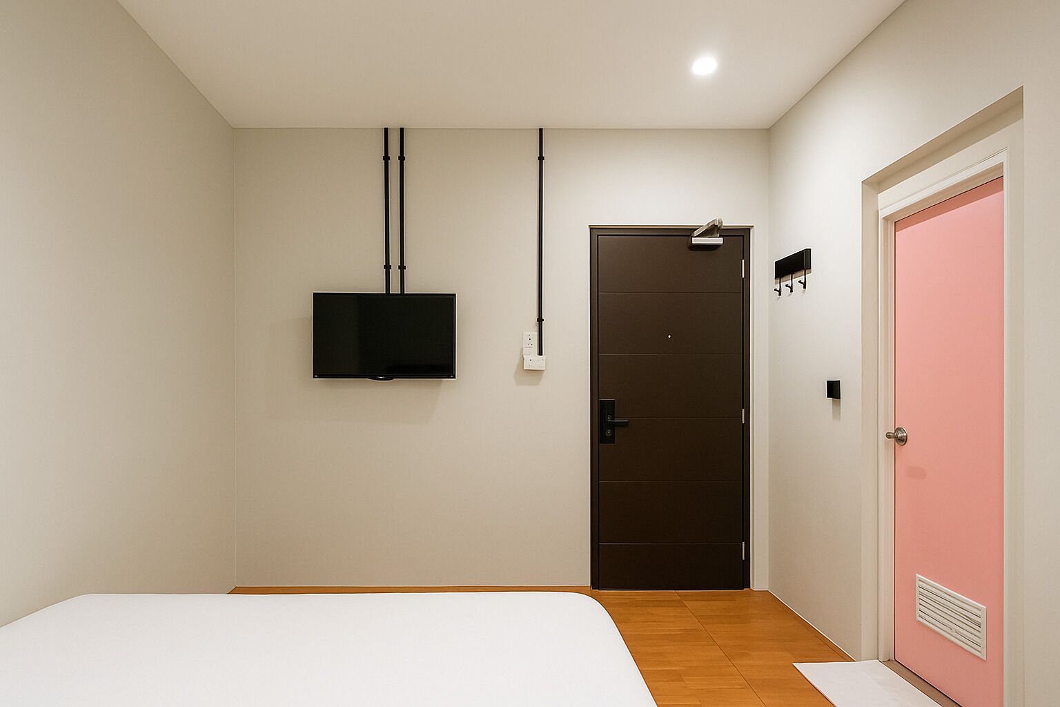 A bedroom with a bed, a television mounted on the wall, a door, and a pink wall.