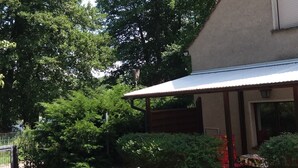 Un espacio al aire libre cubierto con una silla y una mesa de madera, rodeado de vegetación y un edificio.