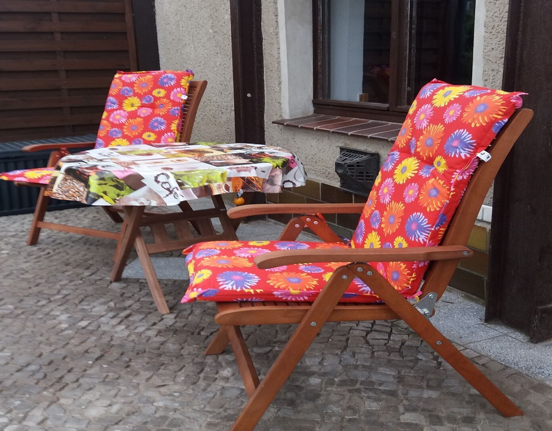 Zwei Holzstühle mit floralem Bezug und ein Tisch mit gemustertem Tischläufer.