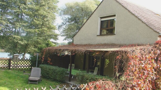 Una casa con techo inclinado, una ventana y un porche cubierto de hiedra.