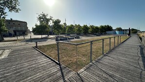 A wooden boardwalk leading to a grassy area with trees and buildings in the background. - Studio COSY - Bath & Netflix - Ideal couple (Pauillac)
