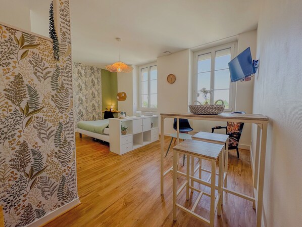 A modern, well-lit room with a bed, desk, and chair, featuring a large window and a decorative wall. - Studio COSY - Bath & Netflix - Ideal couple (Pauillac)