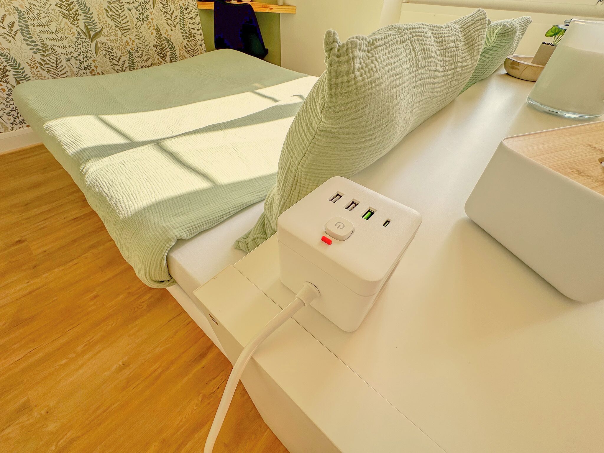 Une chambre bien rangée, avec un lit, une table de chevet dotée d’une multiprise et une petite plante posée sur la table de chevet.