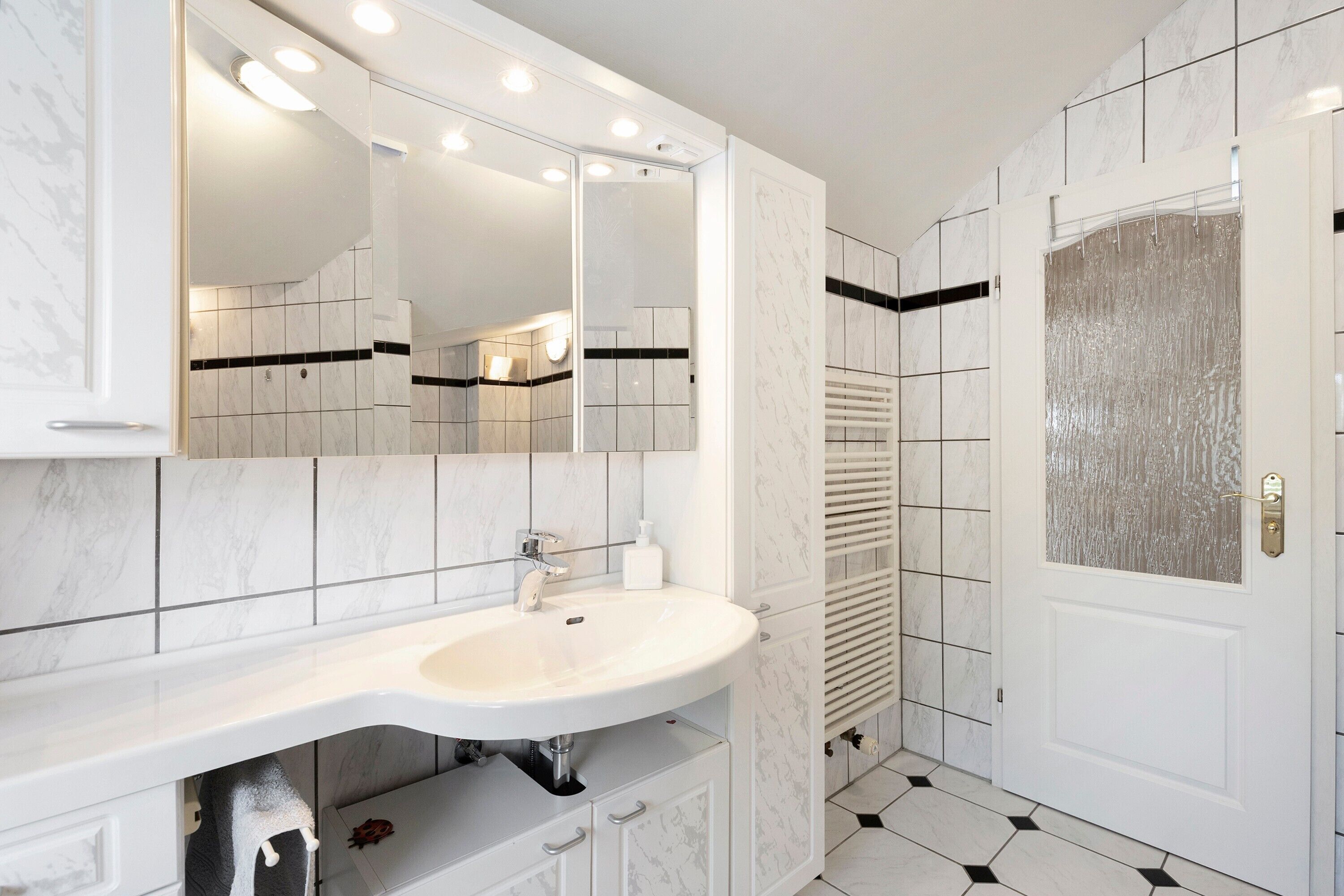 A bathroom with a white sink, mirror, and tiled walls.
