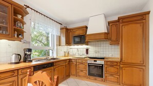 A kitchen with wooden cabinets, a microwave, a coffee maker, and a window with a view of trees.