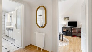 A hallway with a white radiator, a mirror, and a television in a room.